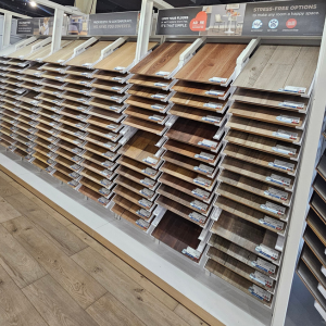 Retail display of wood-look flooring samples arranged by color, with signage highlighting features like waterproof, pet-proof, and scratch-resistant qualities.
